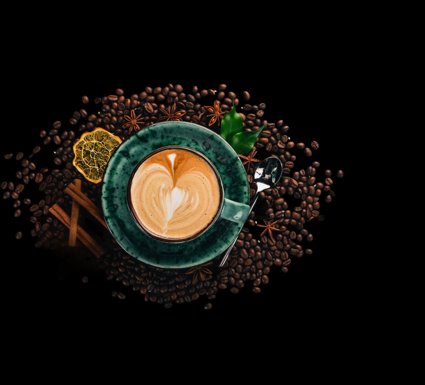 An overhead view of a cappuccino with latte art, surrounded by roasted coffee beans, star anise and cinnamon.